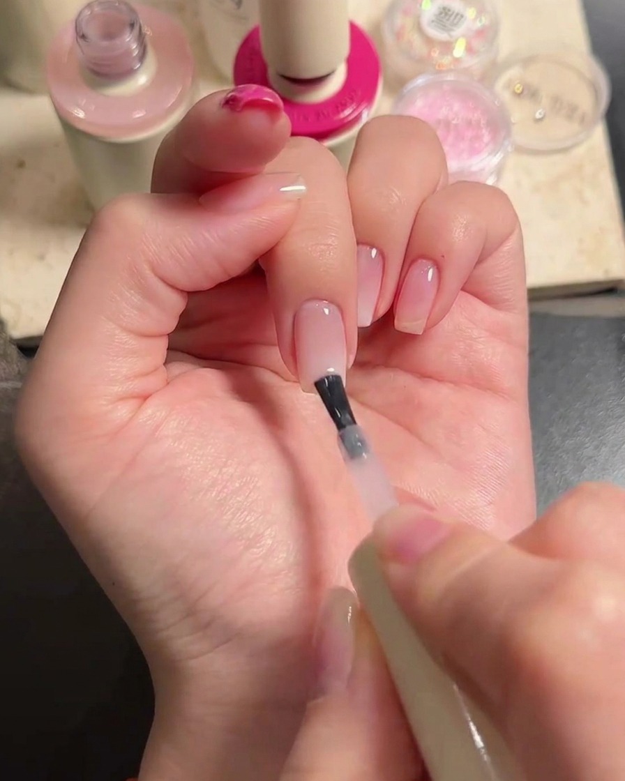 Un pinceau appliquant une couche de gel nude translucide sur les doigts pour fondre le dégradé.