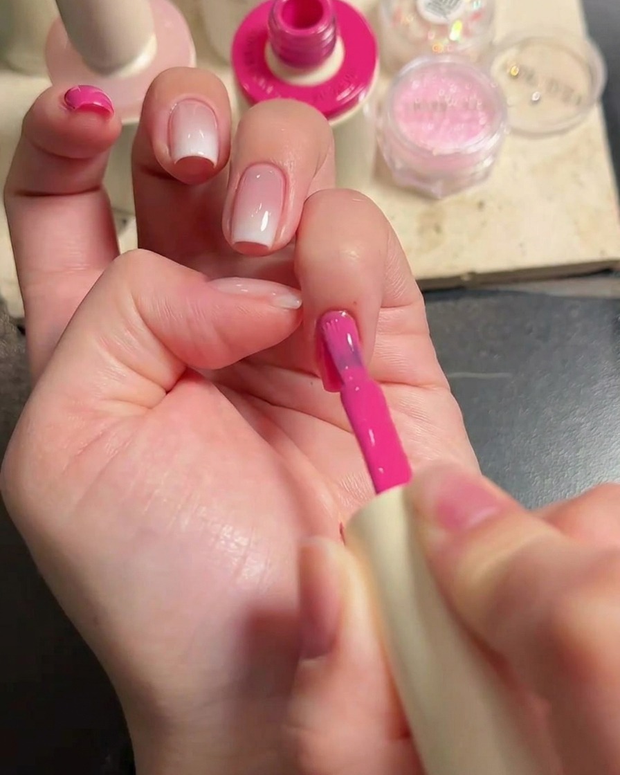 Gros plan dune main avec un pinceau appliquant du gel rose vibrant sur les ongles.