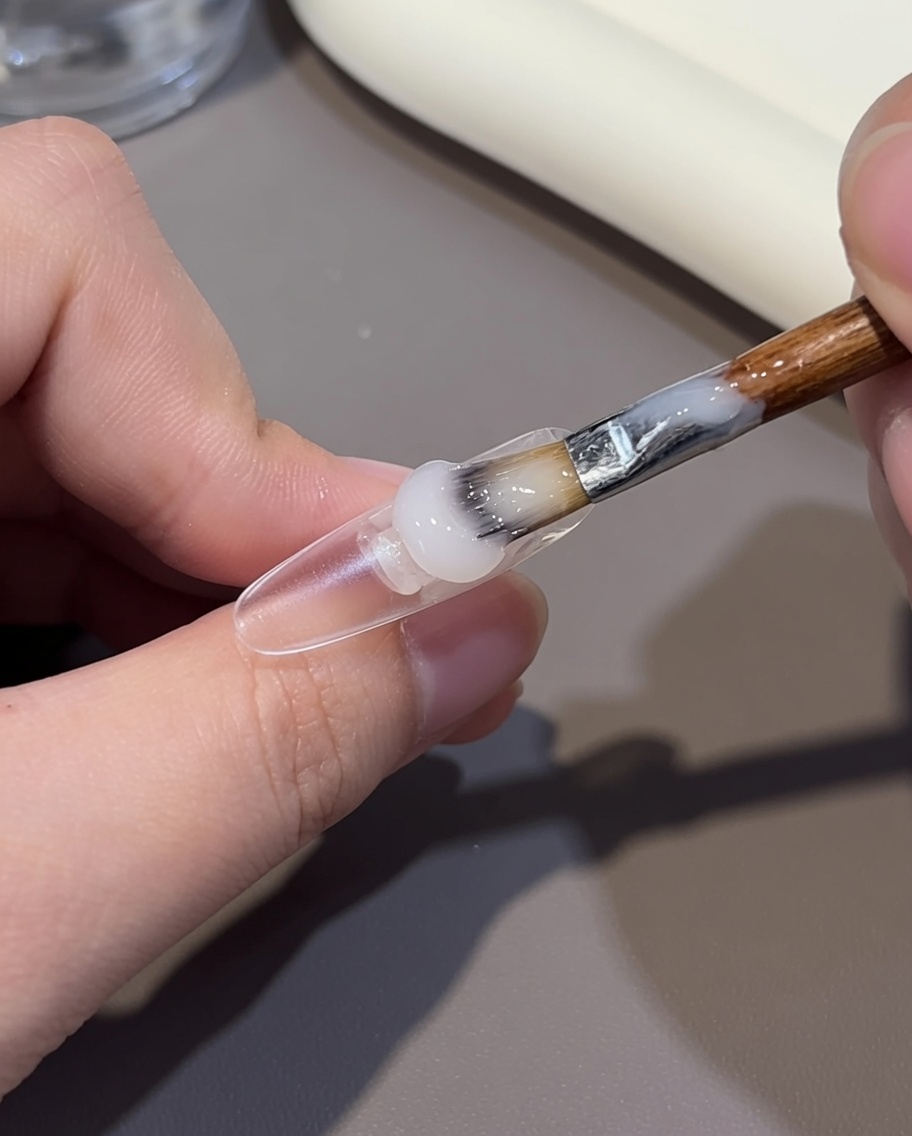 Gros plan dun pinceau appliquant un gel nude sur la moitié postérieure dun ongle.