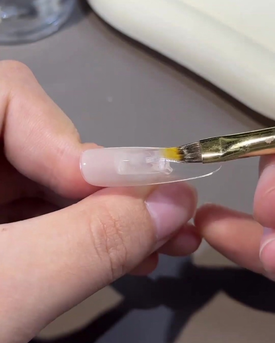 Vue rapprochée dun pinceau estompant légèrement le gel nude sur la surface de longle pour créer un effet dégradé.