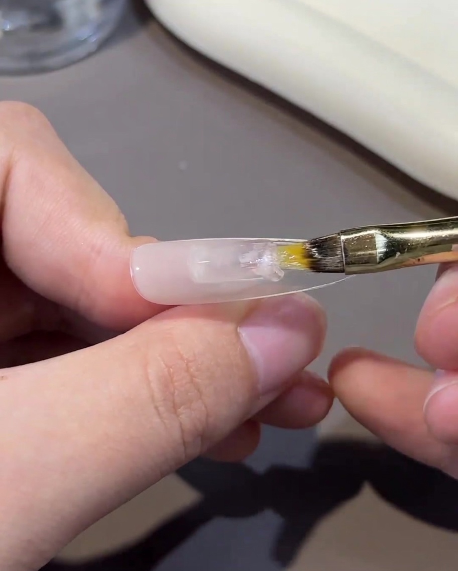 Une main plaçant un ongle sous la lumière dune lampe UV/LED professionnelle.