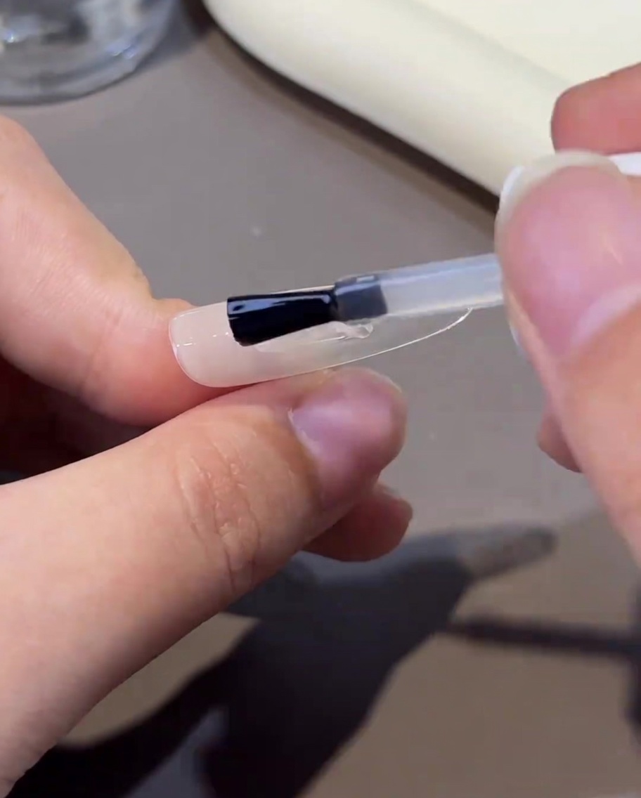 Un pinceau appliquant un gel de renforcement transparent et visqueux sur longle, créant une surface lisse.