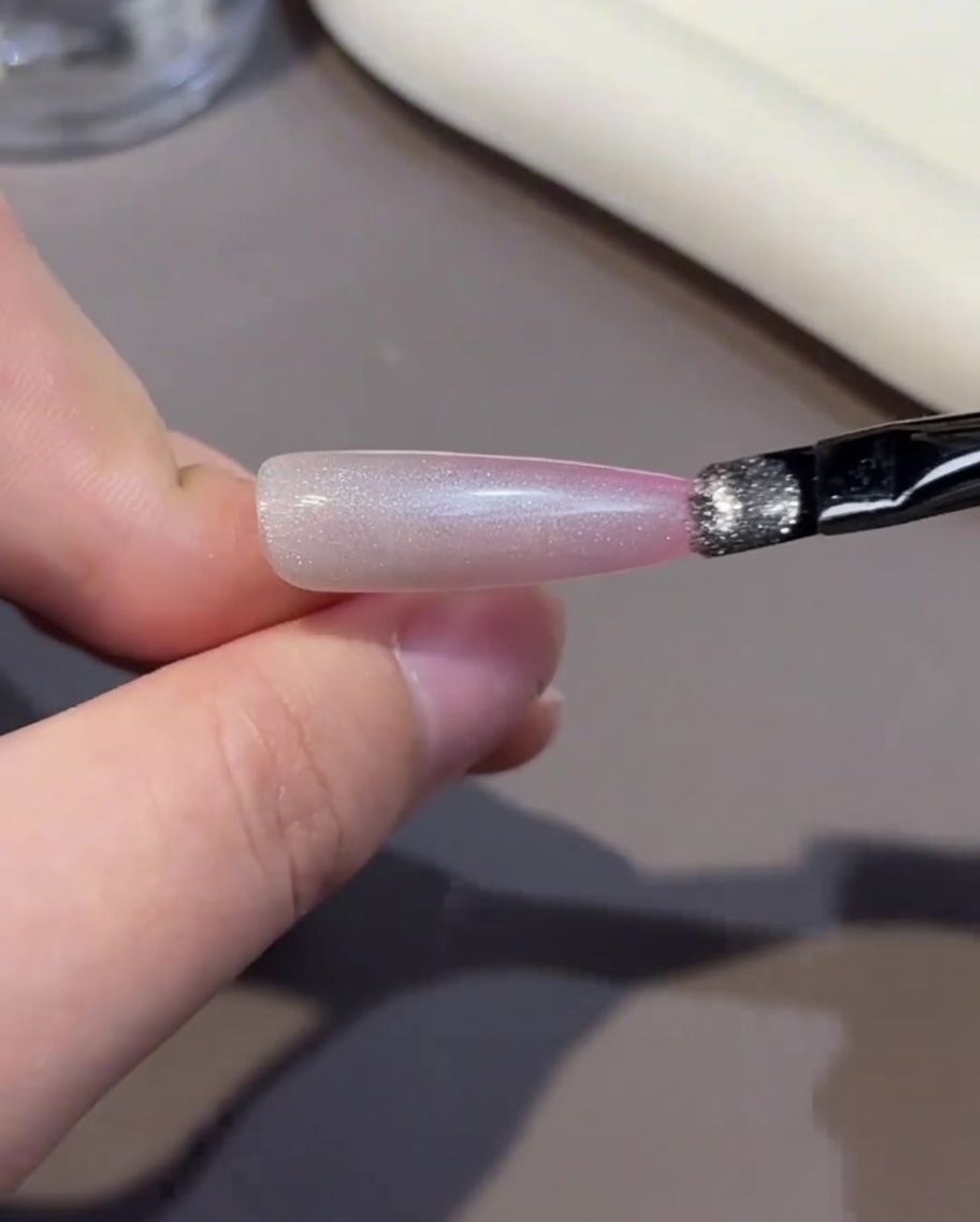Un pinceau appliquant une couche de gel rose sur le bord libre de longle.
