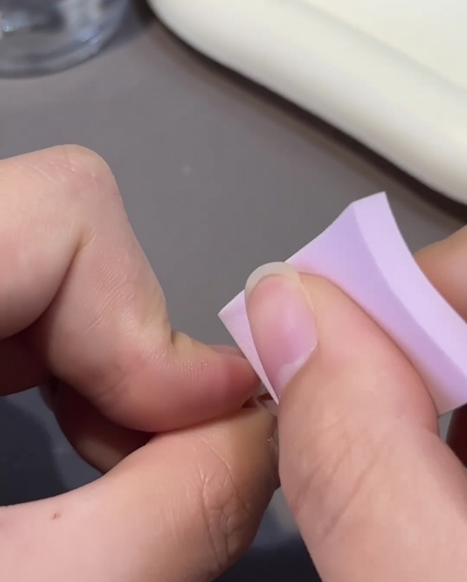 Gros plan dun ongle ombré rose recevant une seconde couche de gel rose à laide dun petit pinceau.