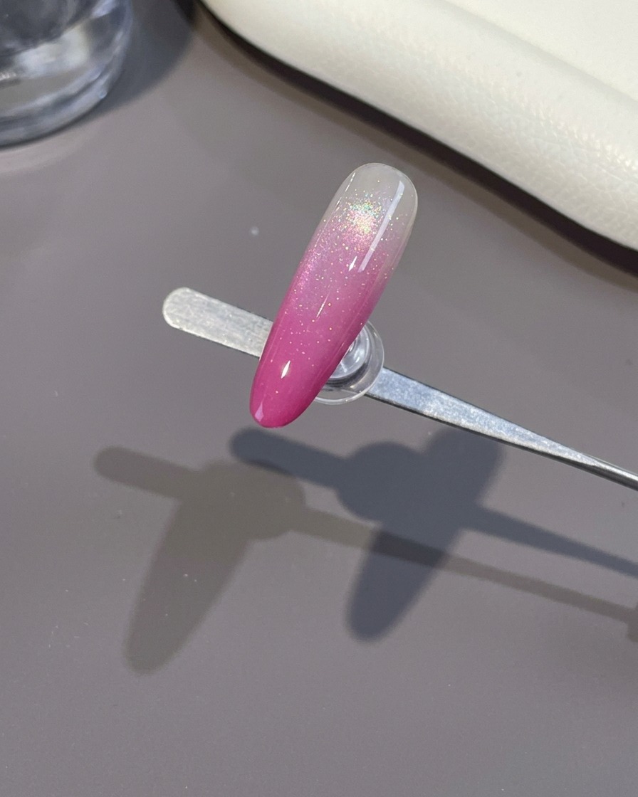 Un pinceau appliquant un top coat brillant sur un ongle ombré rose terminé.