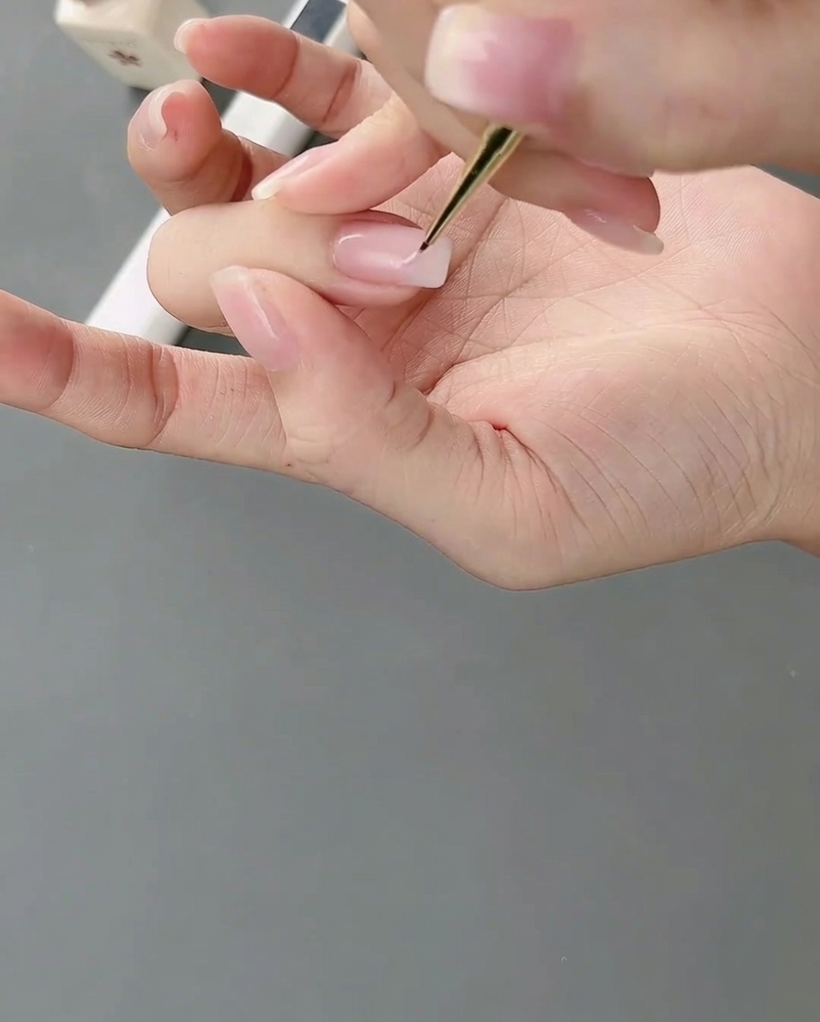 Un pinceau fin de nail art applique du gel rose clair sur un ongle pour former des blocs irréguliers.