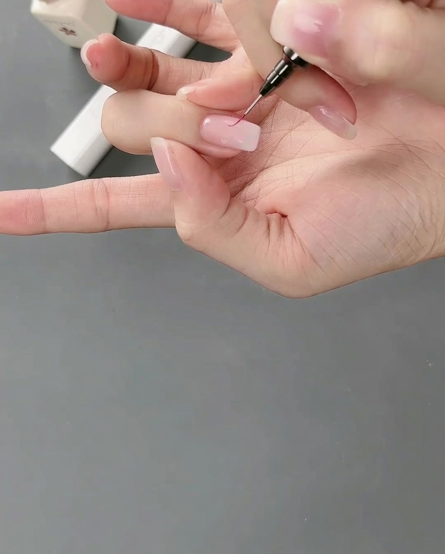 Gros plan dun pinceau liner dessinant des traits fins autour du contour dun bloc de gel rose sur un ongle.
