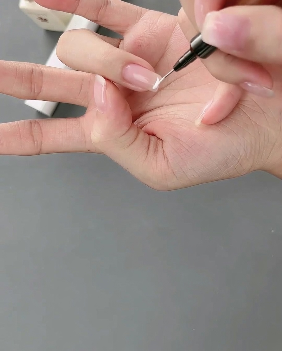 Un pinceau liner appliquant un trait de gel blanc précis pour créer une French manucure haute sur un ongle.