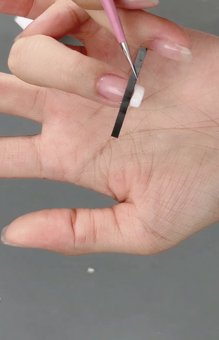 Gros plan dun autocollant pour French manucure positionné sur le bout dun ongle pour créer un guide de grille.