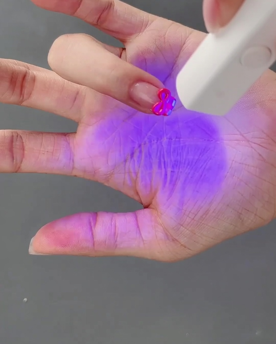 Une main avec un nœud en gel 3D fraîchement sculpté étant catalysé sous une lampe à ongles UV.