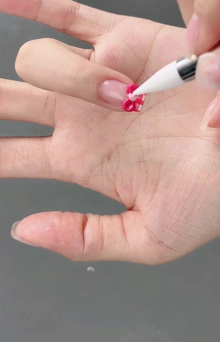 Une petite bille de gel rose clair étant placée au centre dun nœud 3D à laide dun pinceau de détail.