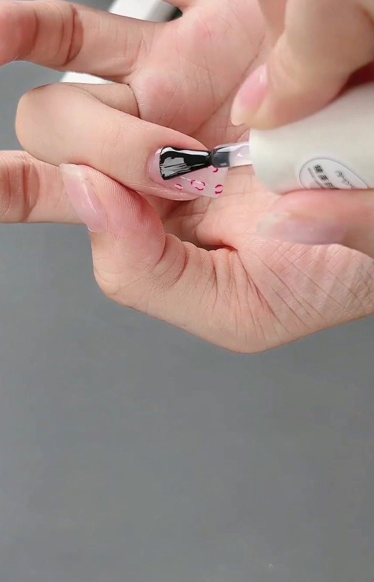 Un pinceau appliquant un top coat brillant final sur le design complet dongle avec French et nœud 3D.