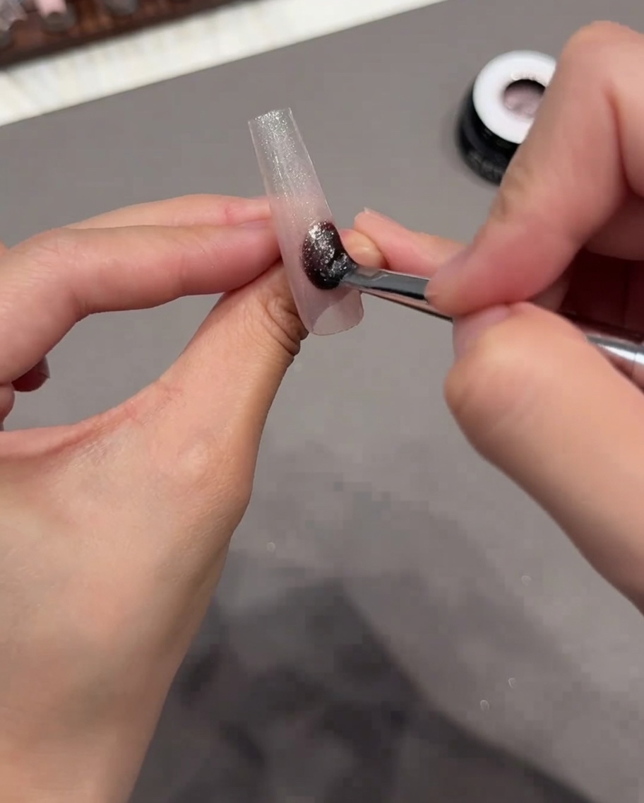 Un pinceau appliquant un vernis gel cat eye scintillant sur toute la surface de la capsule.