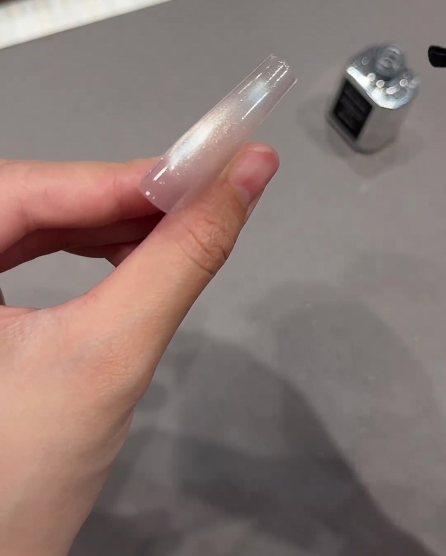 Un pinceau noir appliquant un top coat transparent sur une extension dongle en gel cat eye parfaitement catalysée.