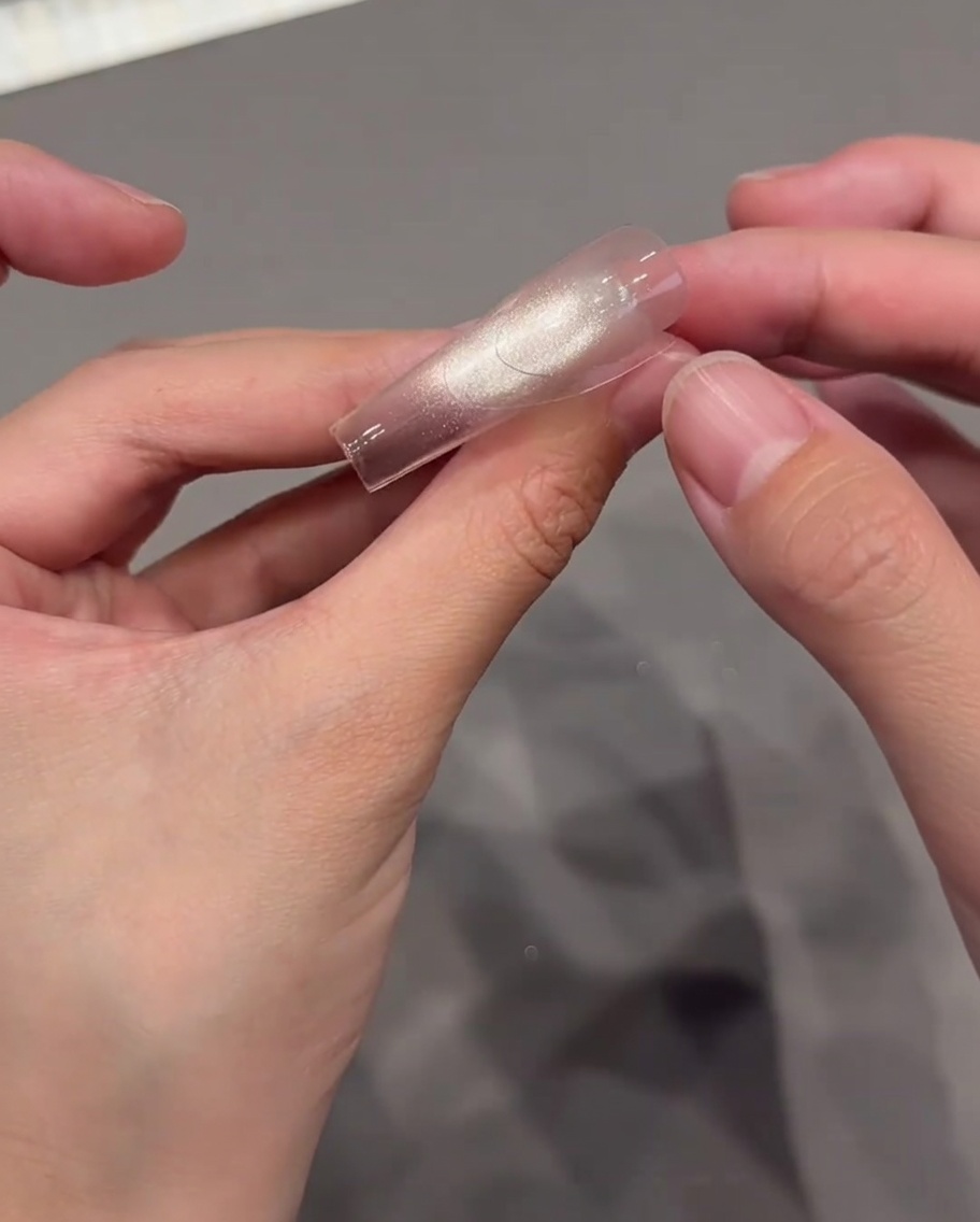 Des pouces plaçant soigneusement un autocollant guide de French manucure incurvé et transparent sur un ongle brillant et pailleté.