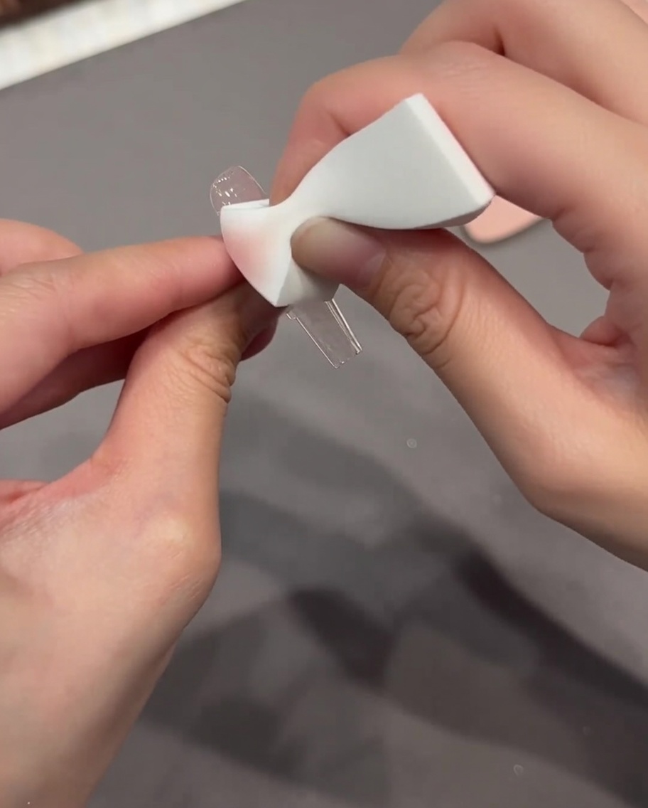 Une éponge utilisée pour presser et fondre un autocollant Chrome Heart sur la surface dun ongle.