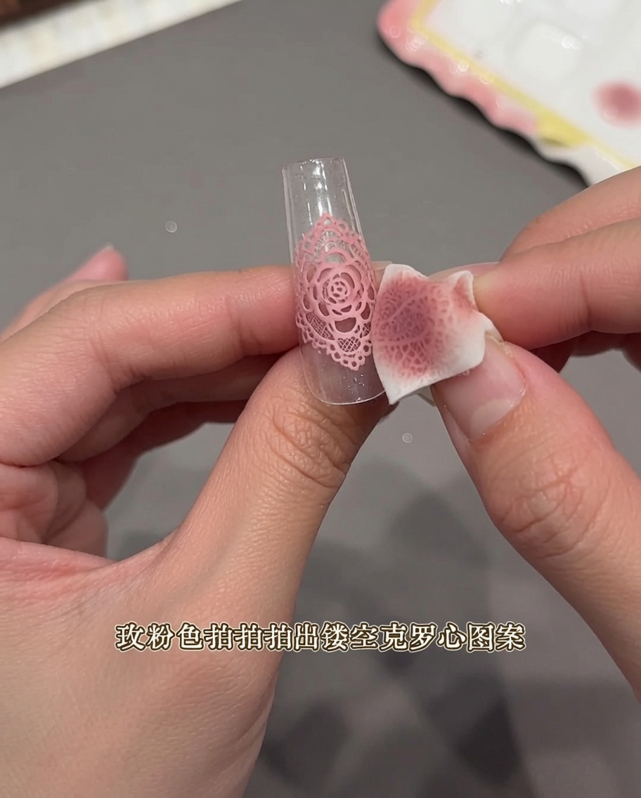 Gros plan dune main utilisant une petite éponge à maquillage pour tamponner un autocollant en dentelle sur une capsule transparente.