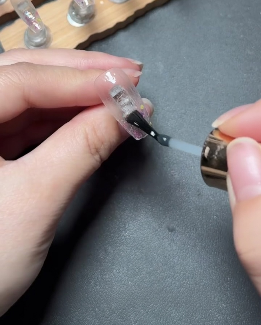 Application dun gel de renfort transparent et épais sur la pointe de longle recouverte de paillettes.