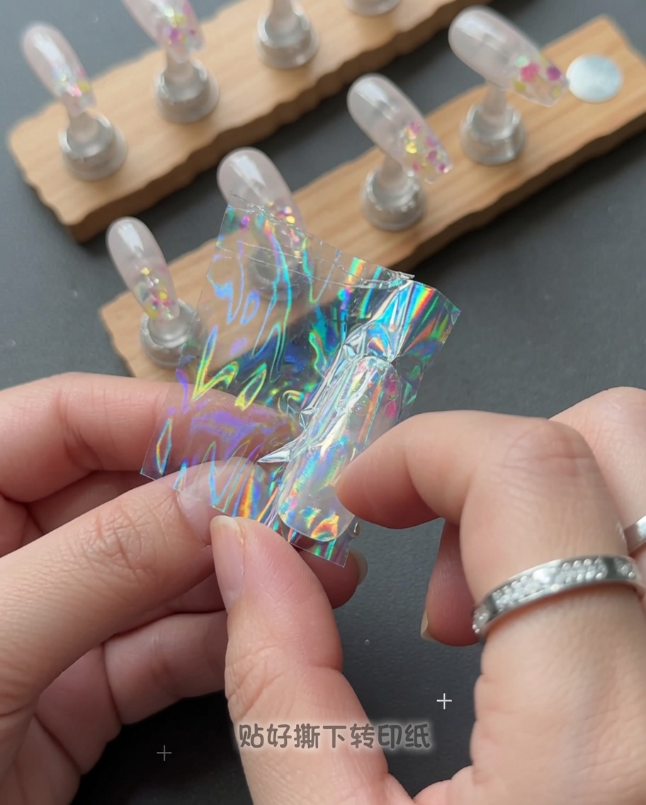 Une main décollant un film plastique transparent dun ongle pour révéler un motif détoile holographique.