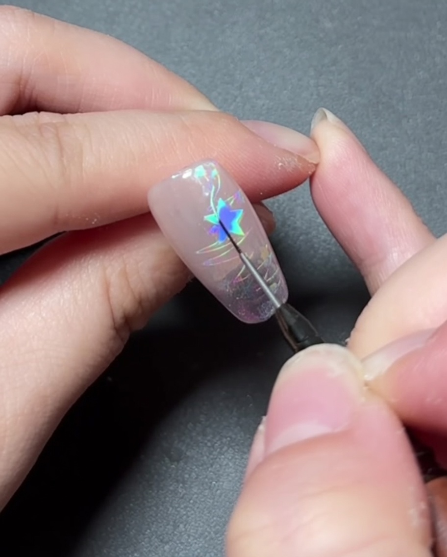 Un pinceau de détail peignant avec du gel coloré vif à lintérieur dun motif détoile sur un ongle.