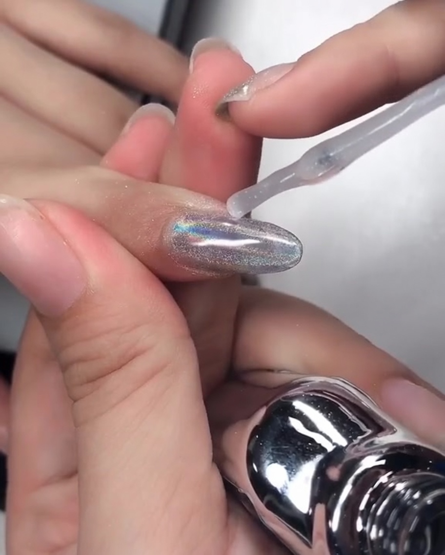 Un pinceau à ongle appliquant un gel de renforcement clair et visqueux sur un ongle chrome, en bordant soigneusement le bord libre.