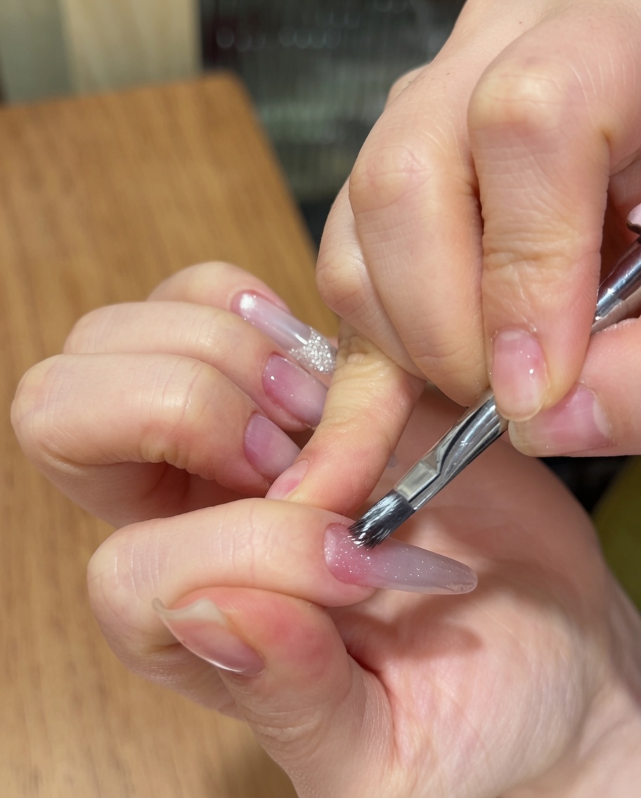 Une main utilisant un pinceau pour appliquer un gel cat eye scintillant sur une base dégradée rose.