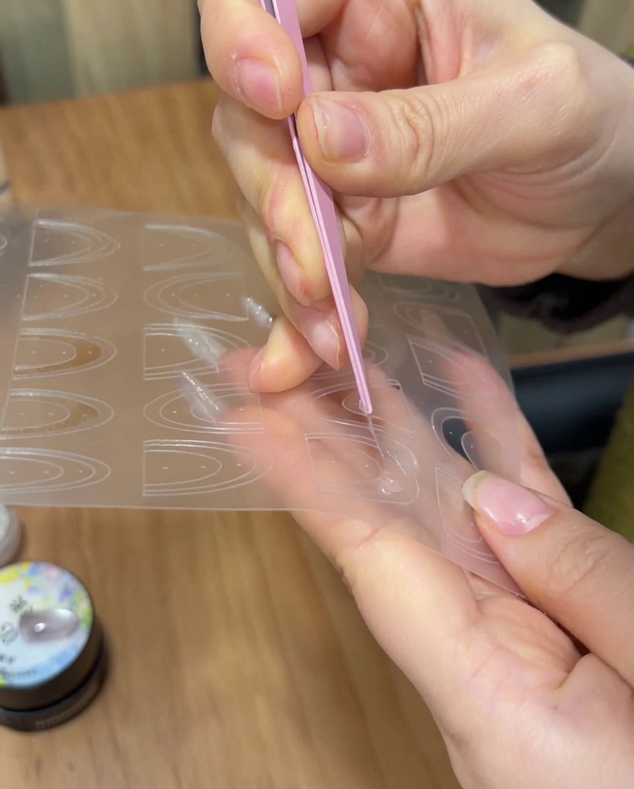 Une pince déposant un autocollant guide de French manucure sur le bout dun ongle.