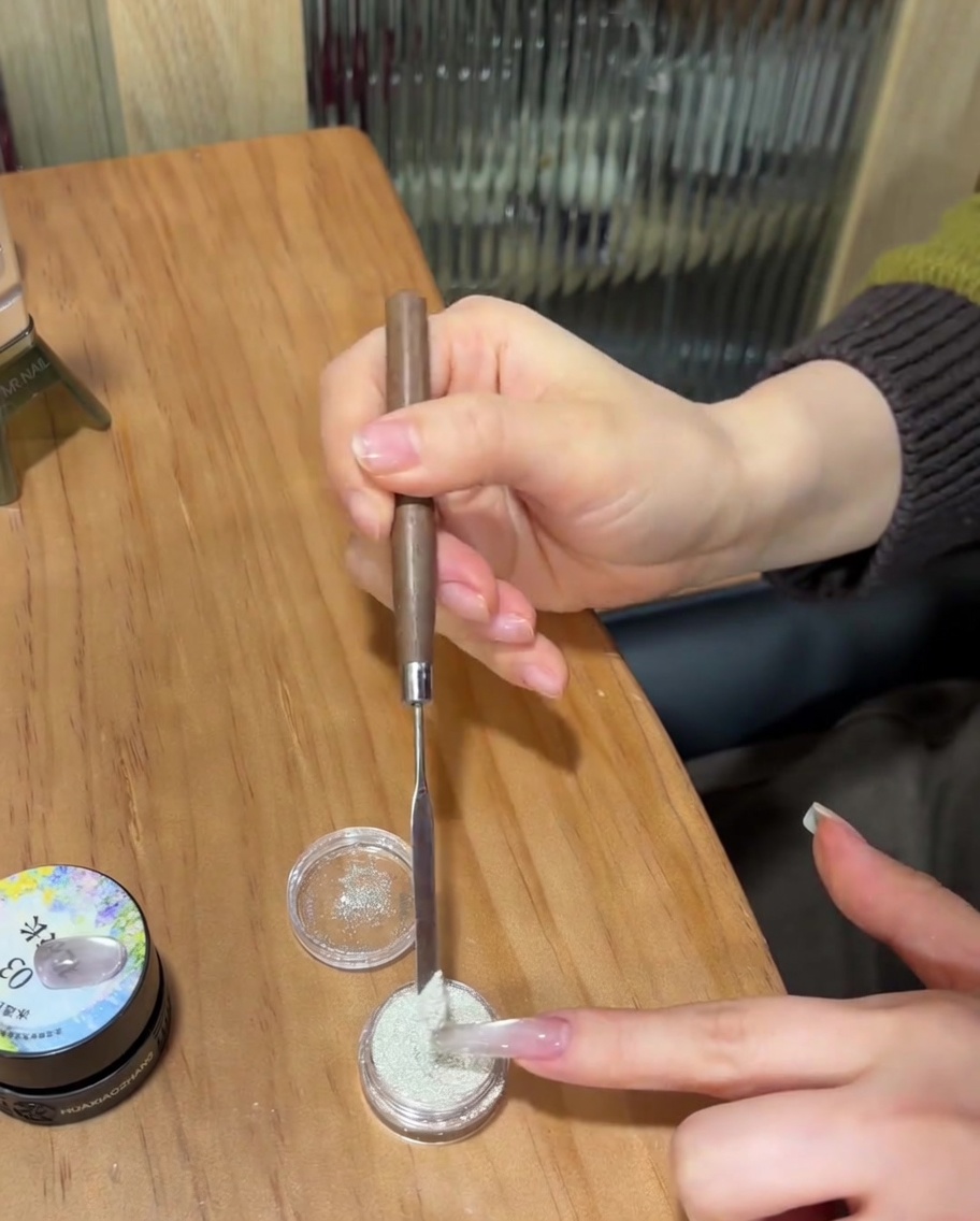 Gros plan dun ongle avec gel clair non catalysé recouvert de poudre blanche fine.