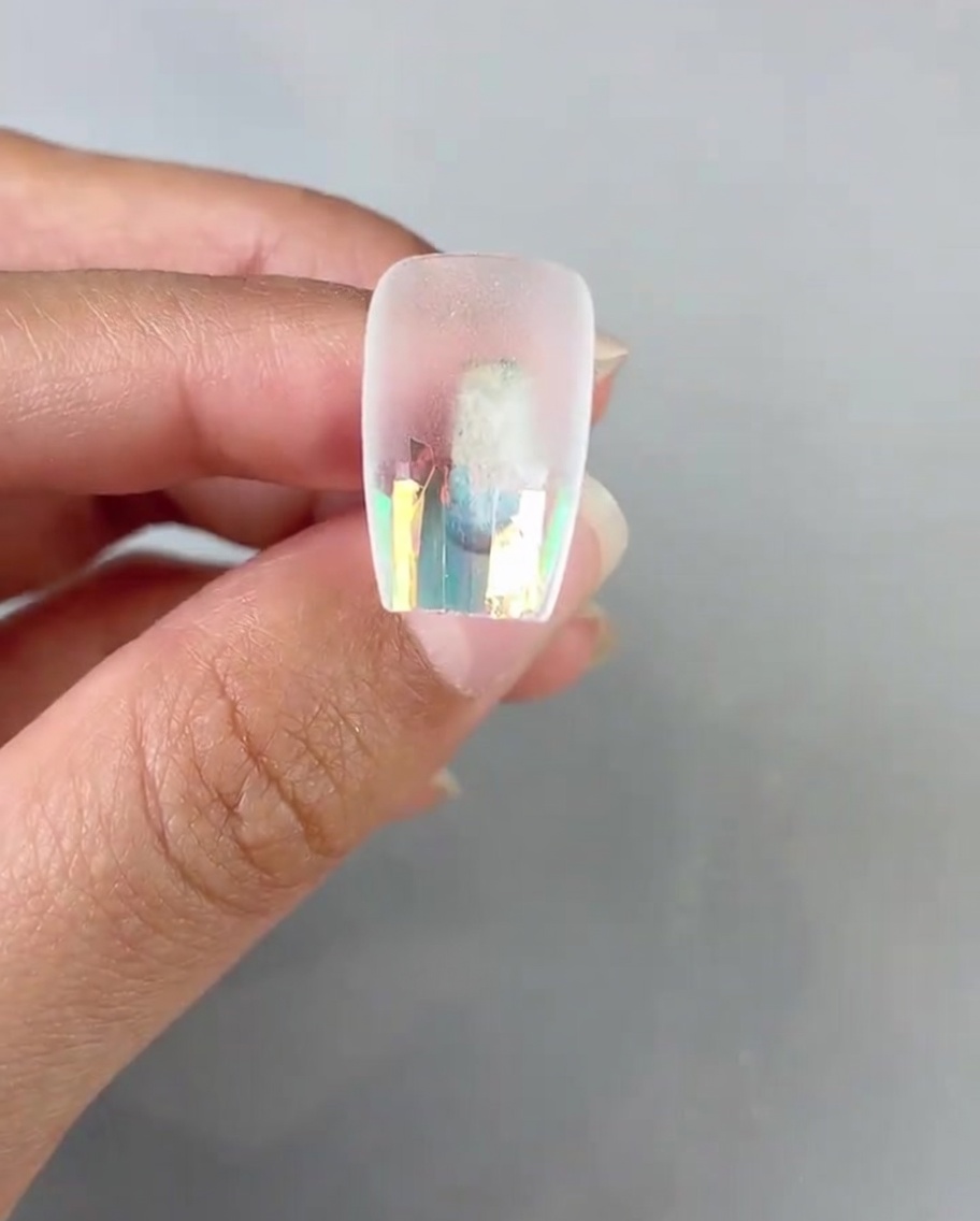 Un pinceau de nail art appliquant une couche de gel de finition transparent sur le papier de verre laser de la capsule.