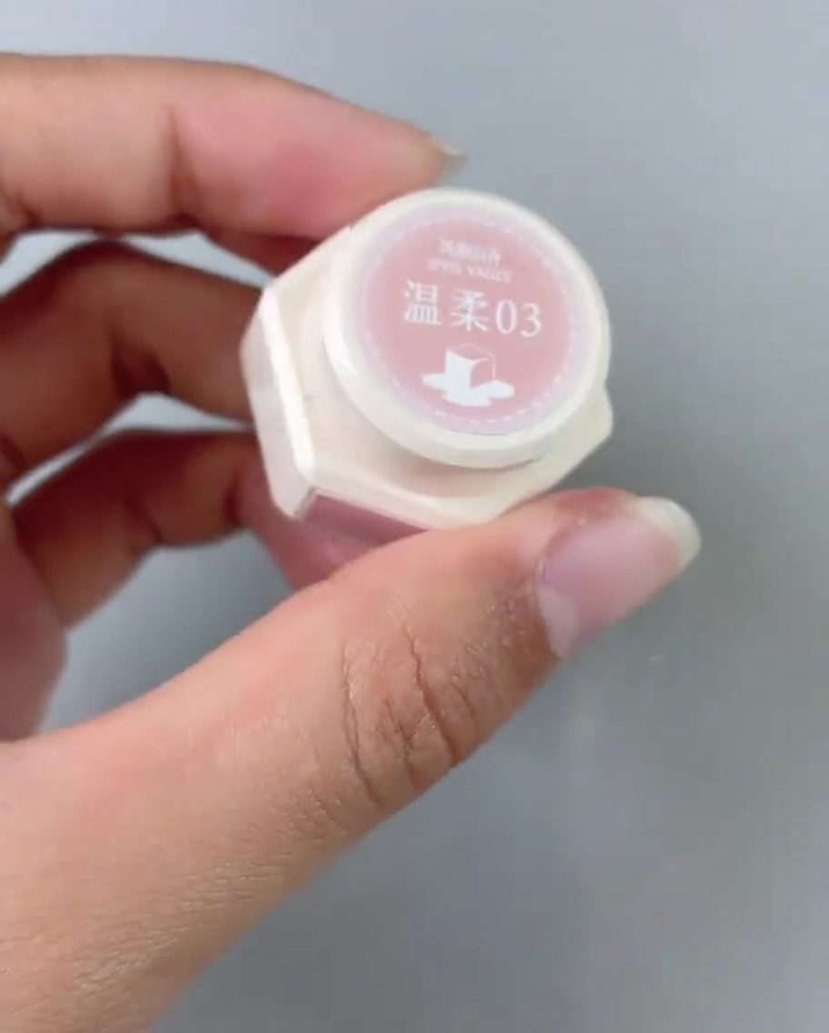 Un pinceau appliquant une couche de vernis gel rose sur la base dune capsule.