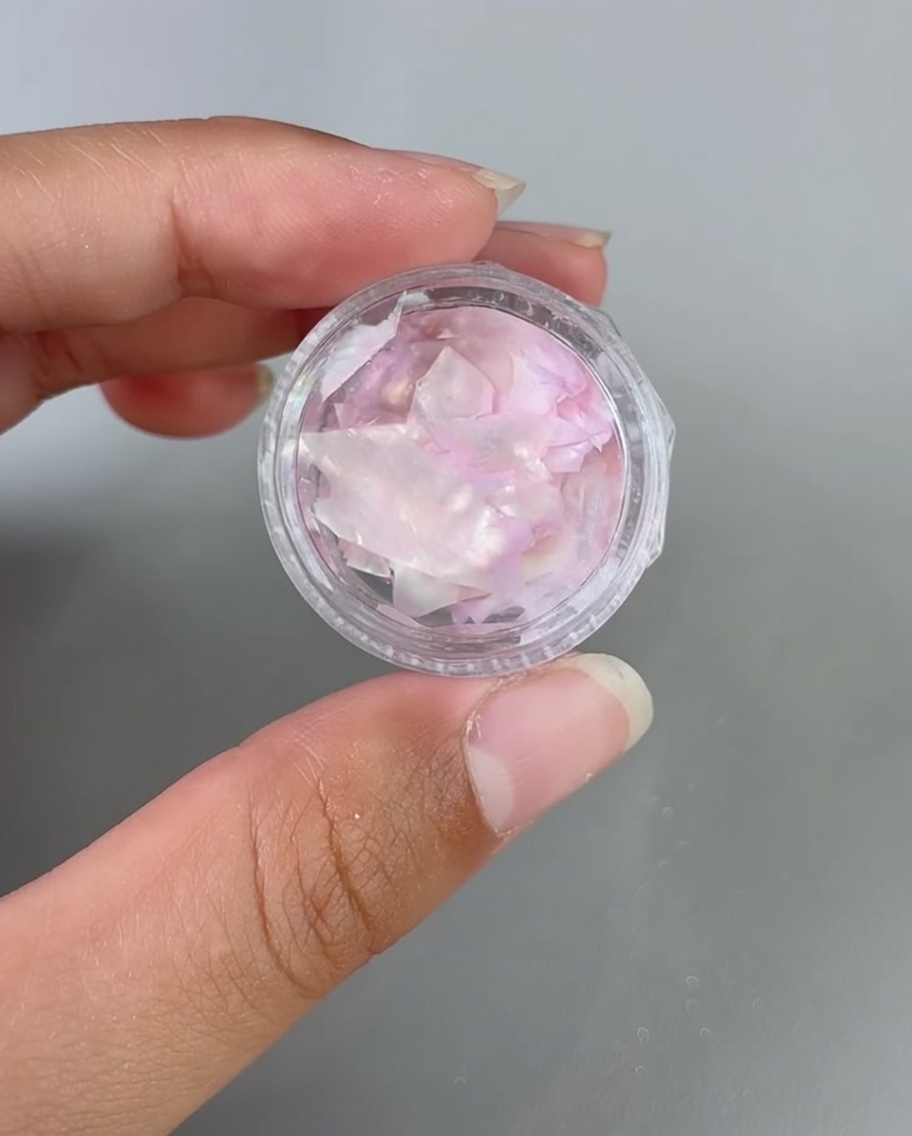 Des pinces plaçant des fragments de coquillage irisés sur un ongle recouvert de gel.