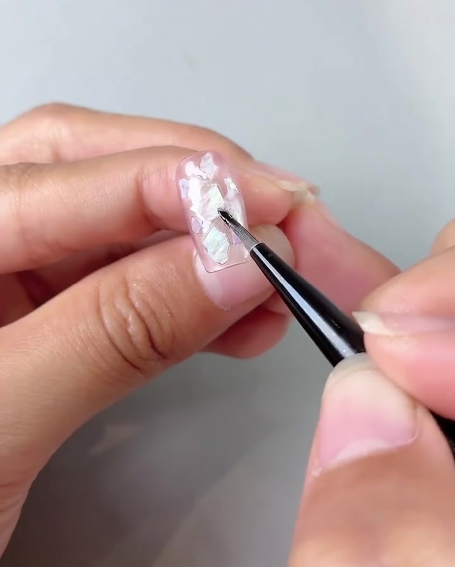 Un pinceau estompant du gel blanc lacté dans les coins dun ongle œil de chat rose.