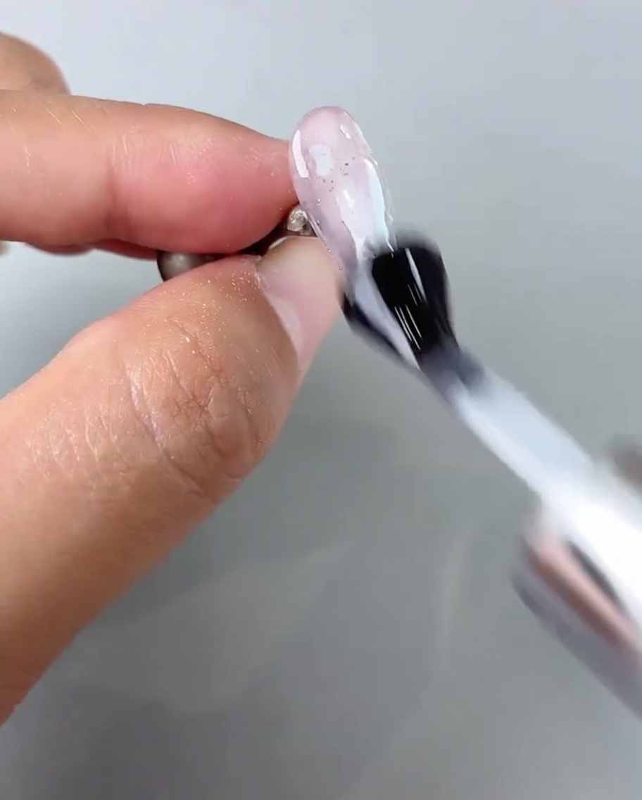 Un pinceau appliquant une couche de finition brillante sur le nail art terminé.