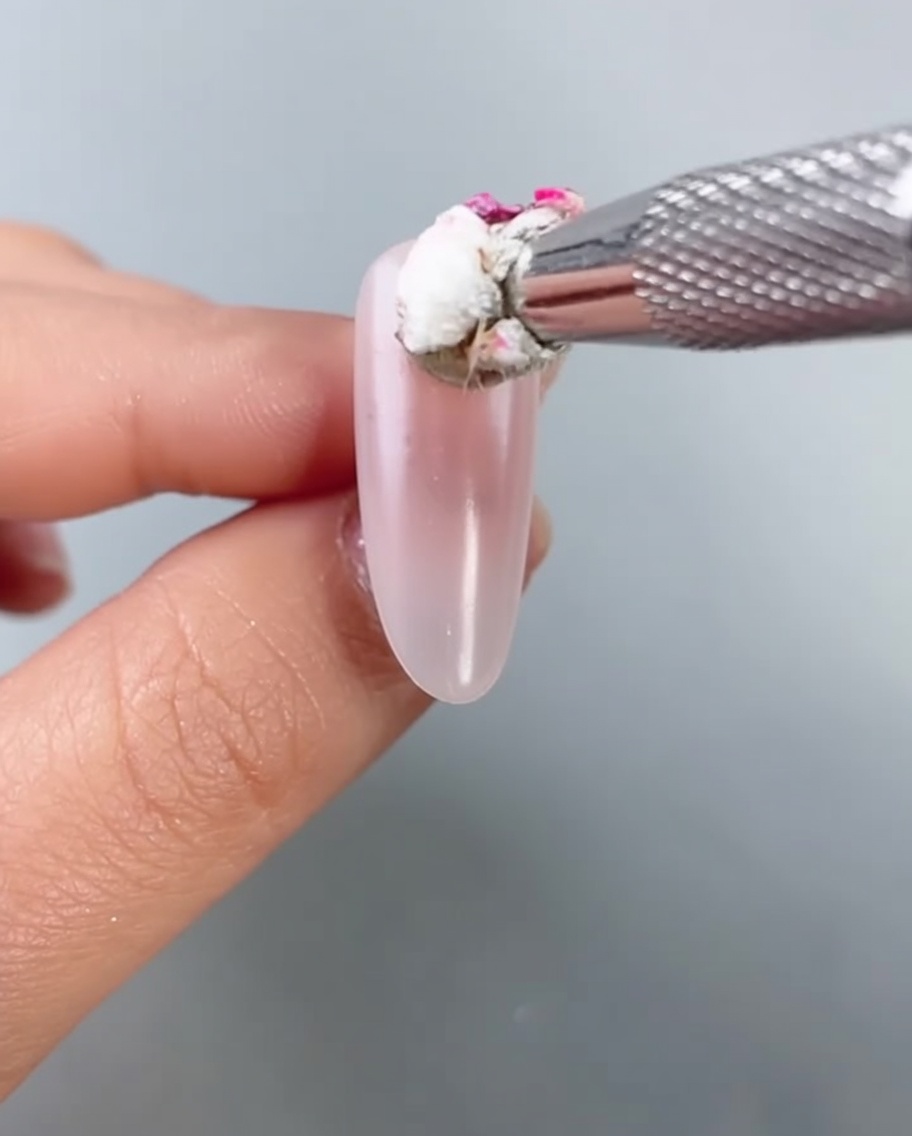 Un gros plan sur une petite éponge tapotant du gel rose vif au centre dun ongle en amande pour créer un effet blush diffus.