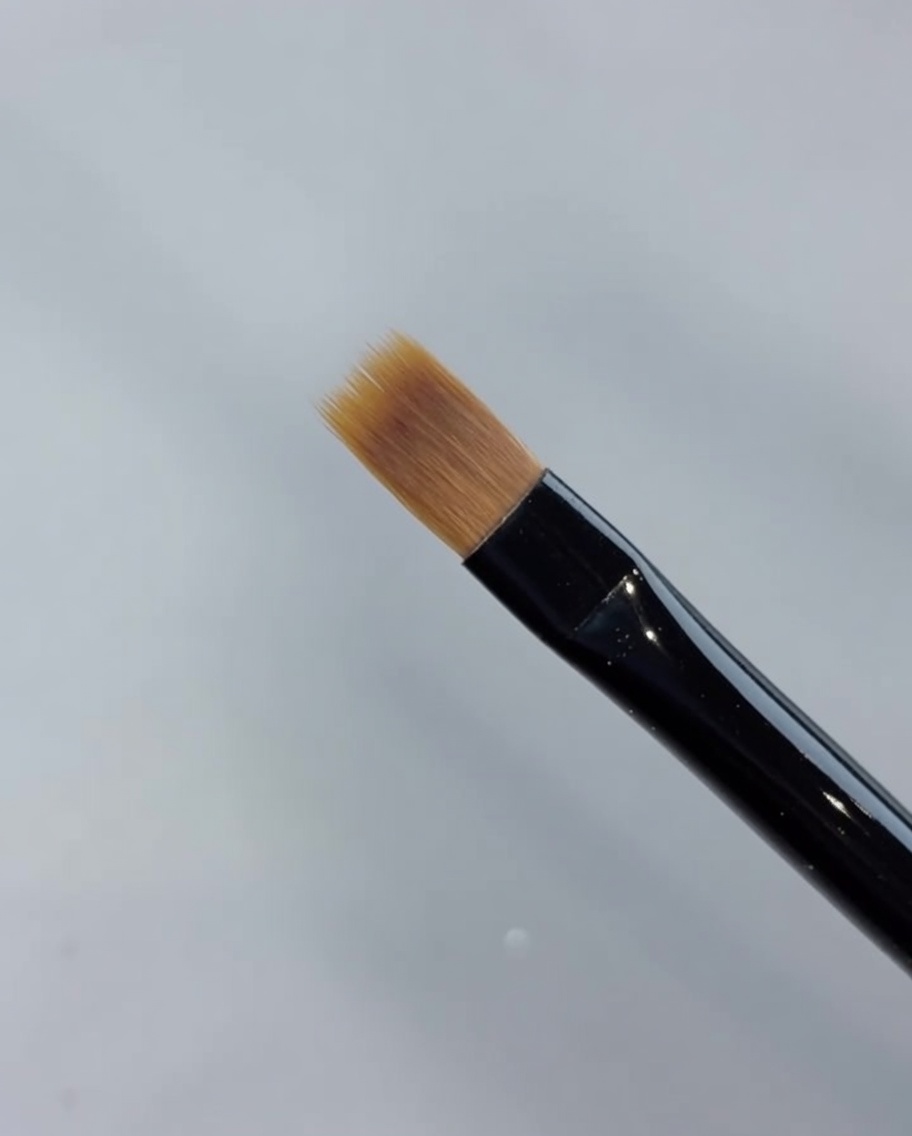 Gros plan dun pinceau balayeur étirant le vernis gel vers lavant pour créer un dégradé.