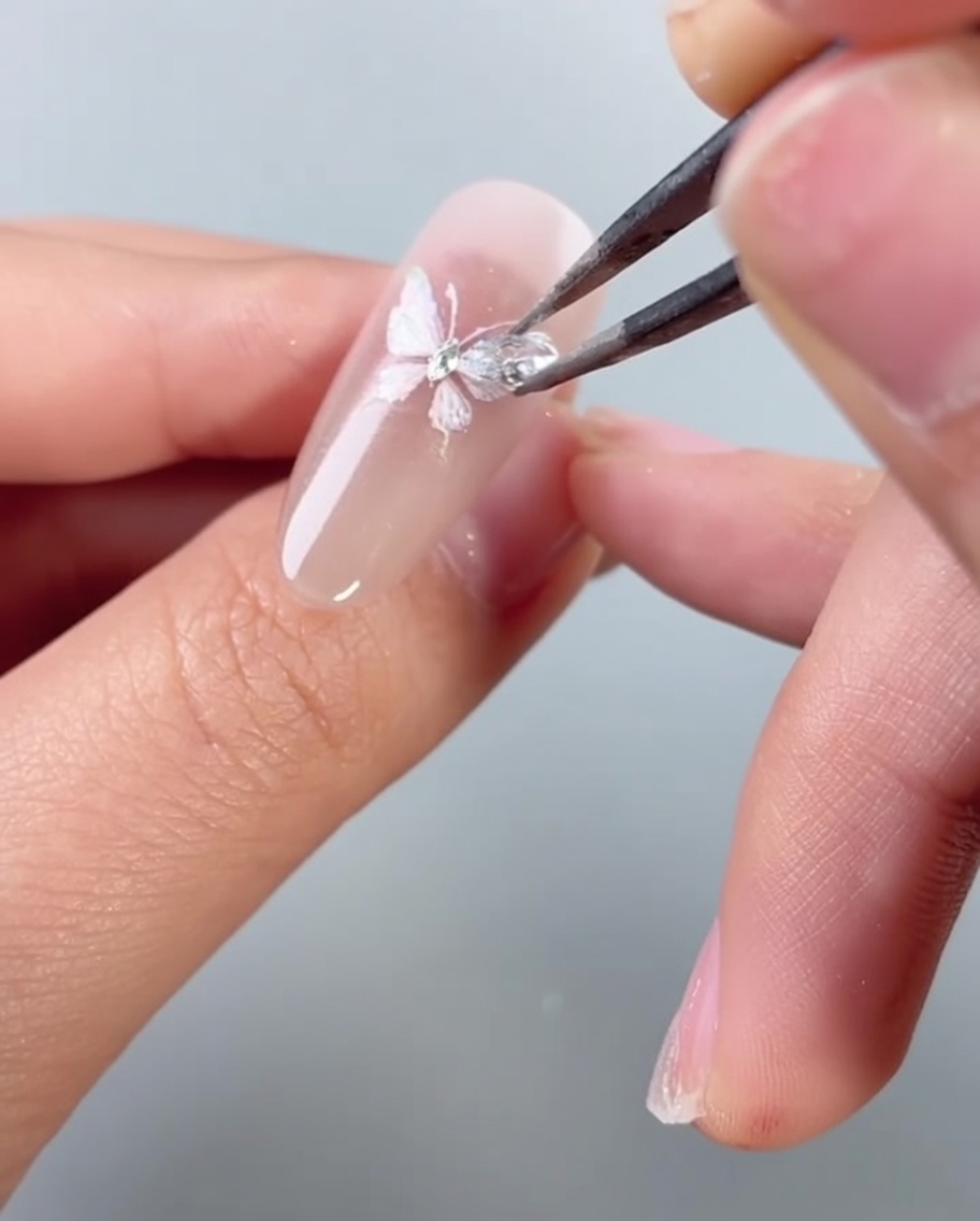 Une pince plaçant un petit strass scintillant sur un motif de nail art papillon.