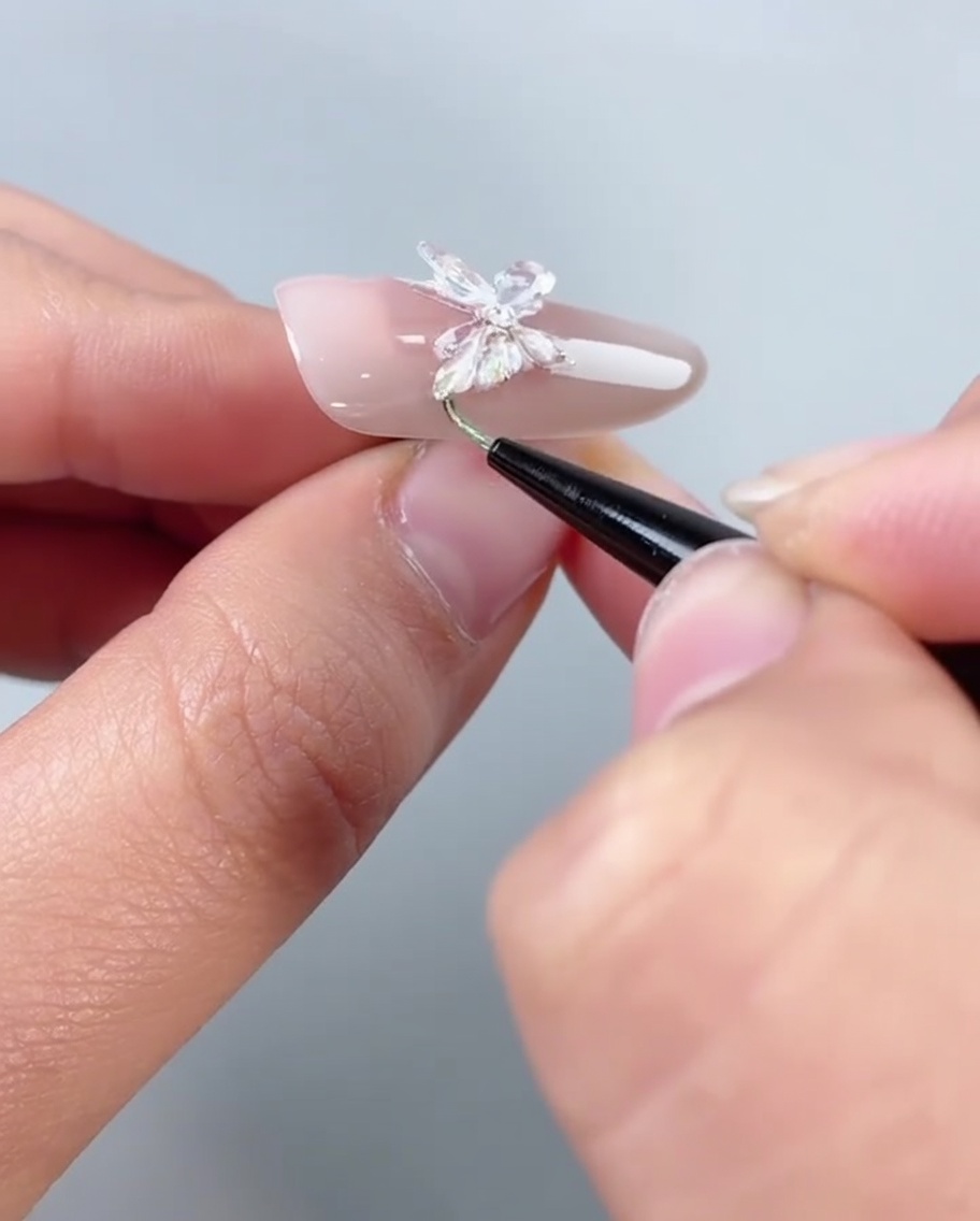 Un pinceau appliquant du gel de remplissage transparent le long du bord inférieur dun ongle décoré dun papillon.