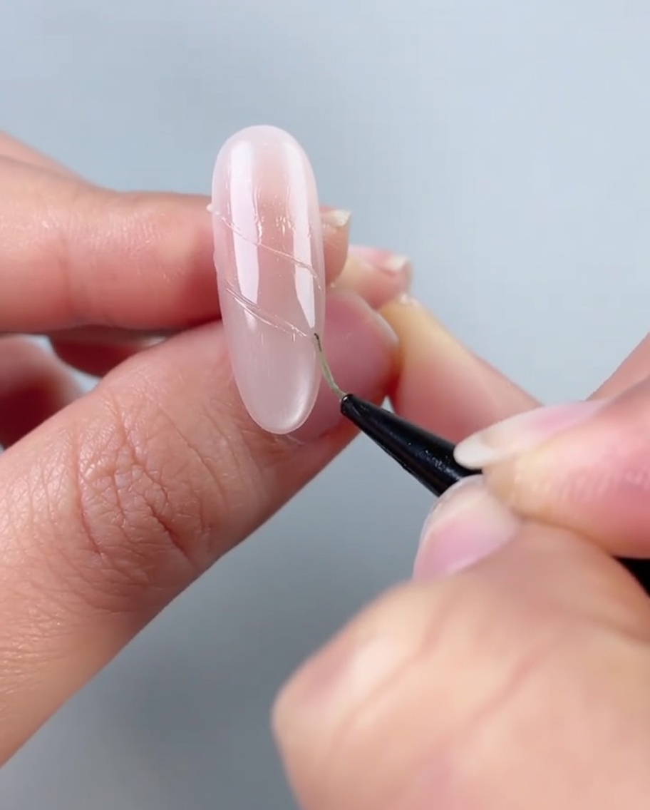 Un ongle montrant une ligne de petites perles blanches et de strass transparents placés sur des lignes de colle adhésive.