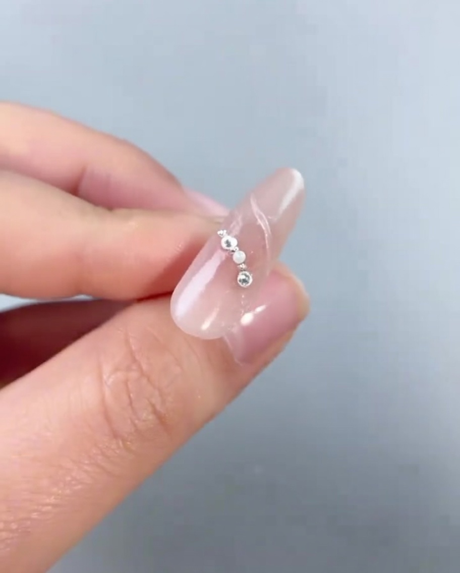 Gros plan dun bijou en forme de pentagramme argenté placé sur un ongle décoré de petites perles et billes.