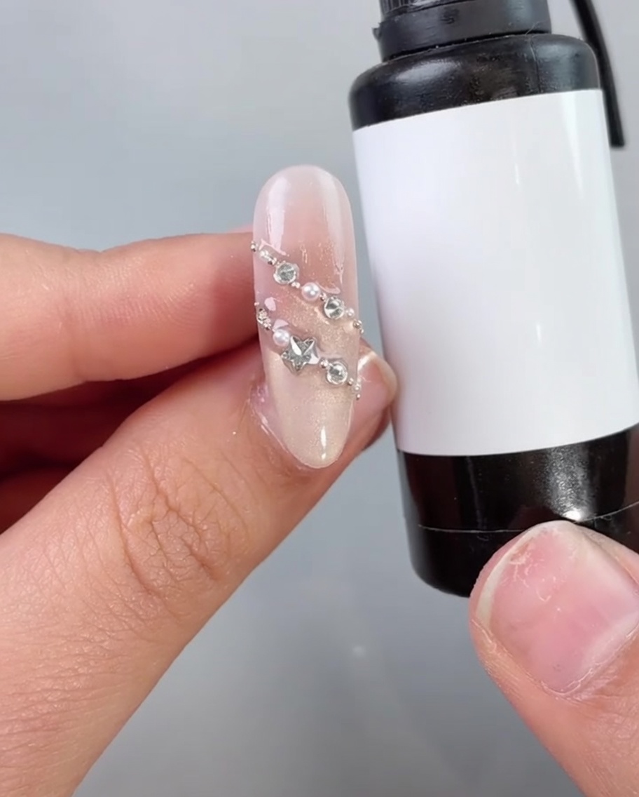 Un pinceau appliquant un top coat transparent ou un scellant sur un ongle décoré de perles et de strass.