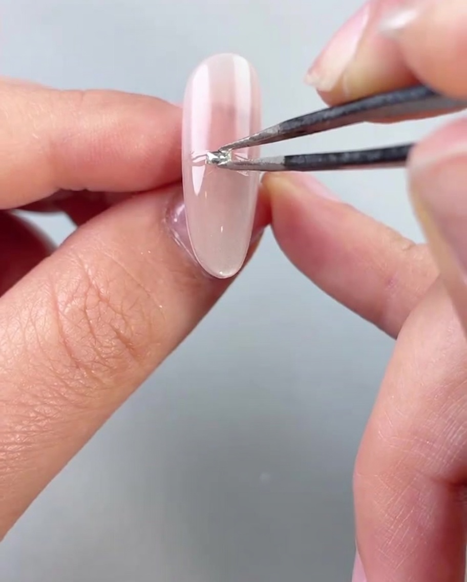 Une pince plaçant de petites billes argentées ou des strass horizontalement au milieu dun ongle peint au gel.