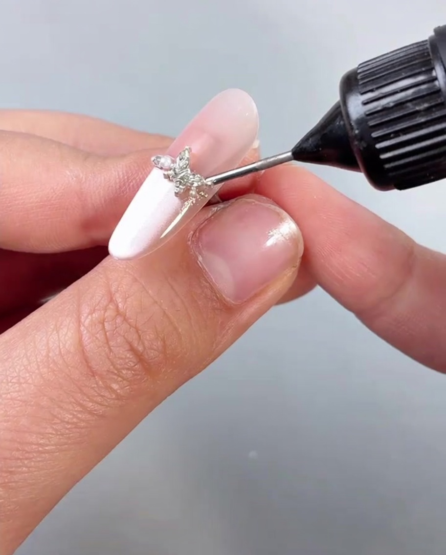 Application dun top coat transparent ou dun scellant sur un ongle orné dun bijou papillon.