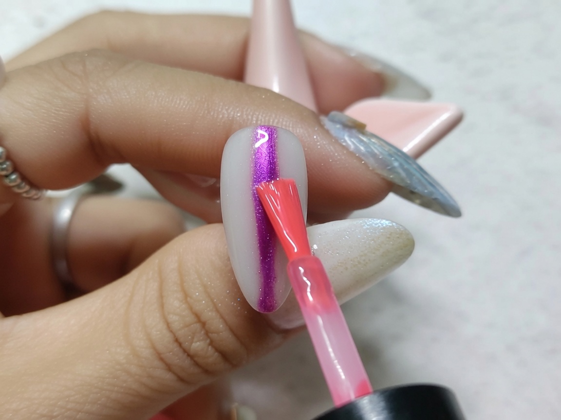 Un pinceau nail art appliquant une bande verticale dencre aquarelle rouge vif au centre dun ongle finition métallique.