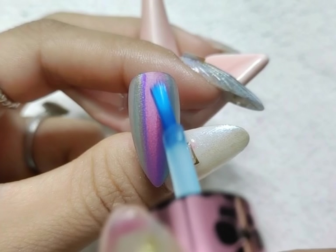 Gros plan dun pinceau estompant délicatement les bords humides des encres rouge et bleue sur un ongle chrome.