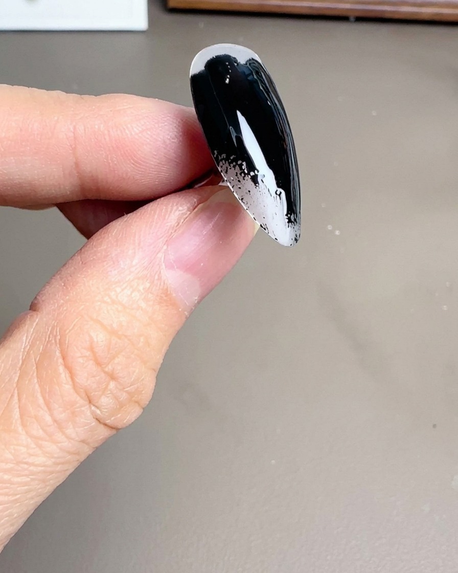 Gros plan dun pinceau appliquant un vernis gel noir brillant sur un ongle stiletto.