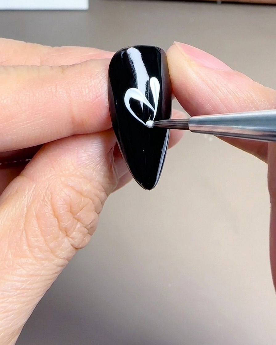 Gros plan dun pinceau liner créant des pétales blancs délicats et allongés sur un ongle noir.