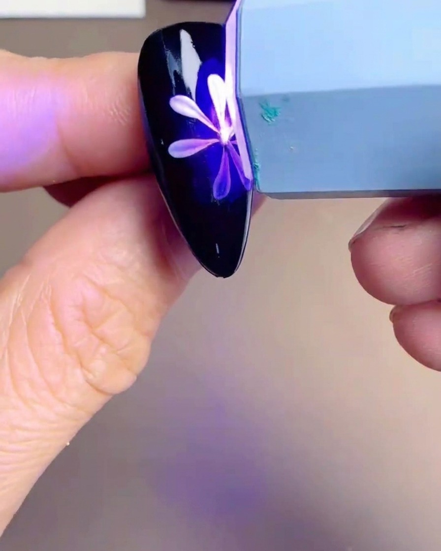 Lampe UV/LED portative au-dessus dun ongle avec un motif de marguerite blanche et jaune.