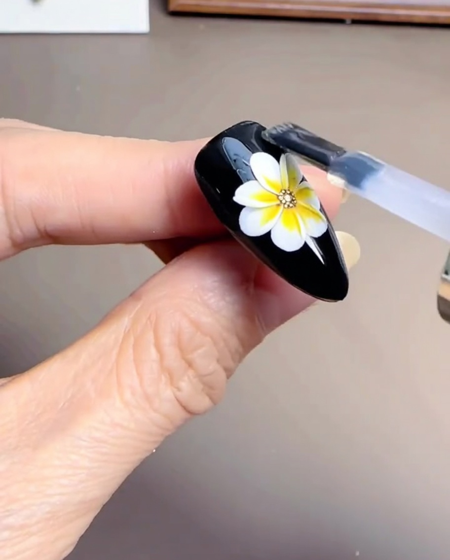 Pinceau appliquant un top coat transparent sur un design de marguerite partiellement terminé.
