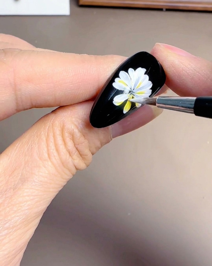 Gros plan dune main ajoutant des pétales blancs superposés sur un ongle noir.