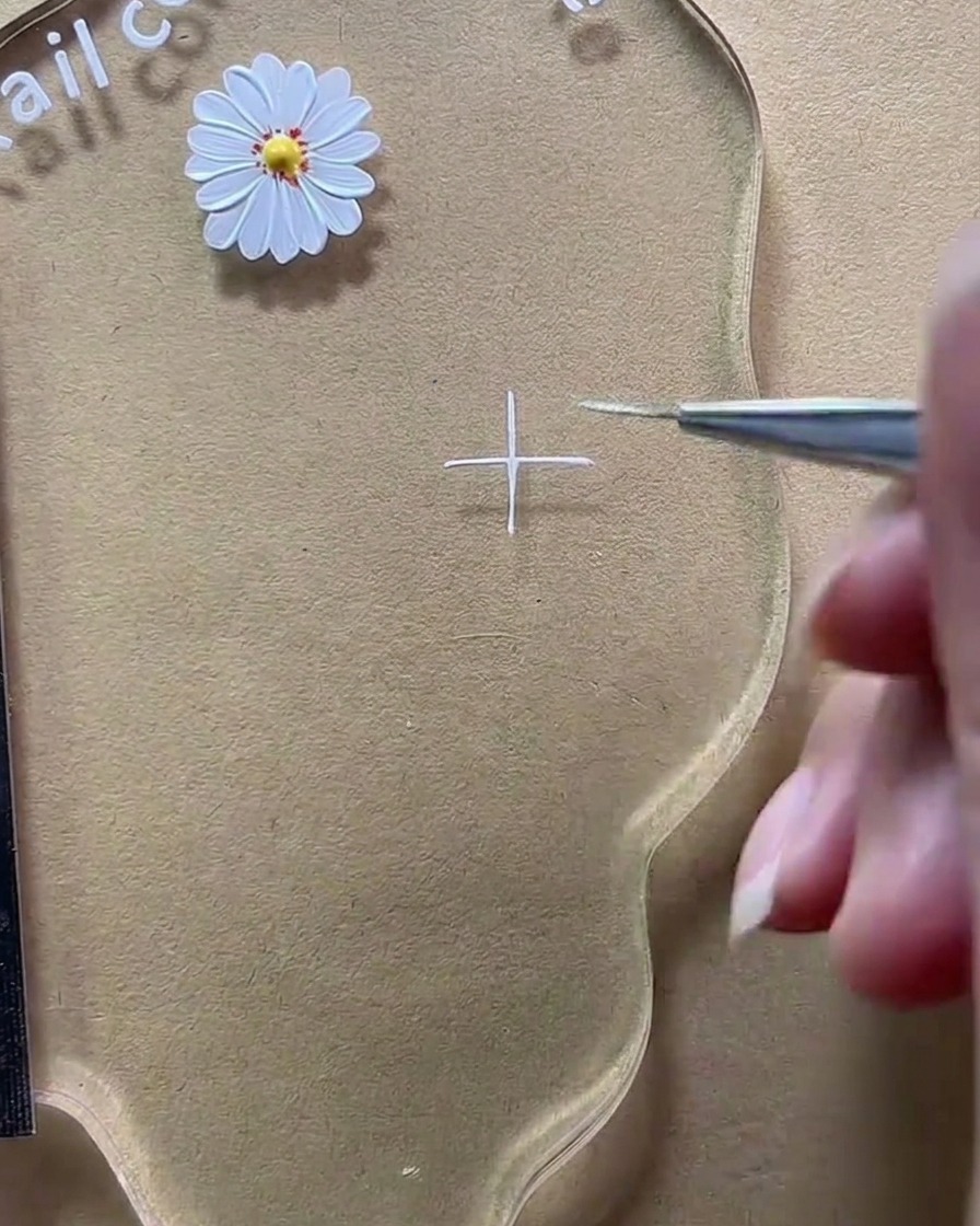 Gros plan dun pinceau liner complétant une croix blanche sur la palette transparente.